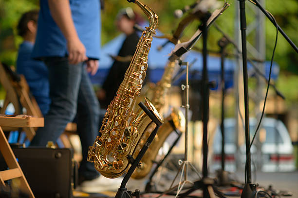 Male Musician in a Formal Black Suit Holds a Tenor Saxophone on the background of the concert atmosphere. Saxophonist Plays Jazz. Saxophone Close-up. Copy space