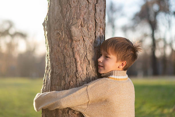 Young boy embracing a tree trunk in a park, demonstrating connection with nature and environmental awareness