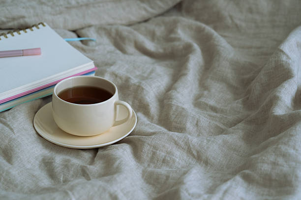 istock coffee or tea in bed with beautiful warm light. Notebook and a pen. Minimal aesthetic still life composition. 2234918222