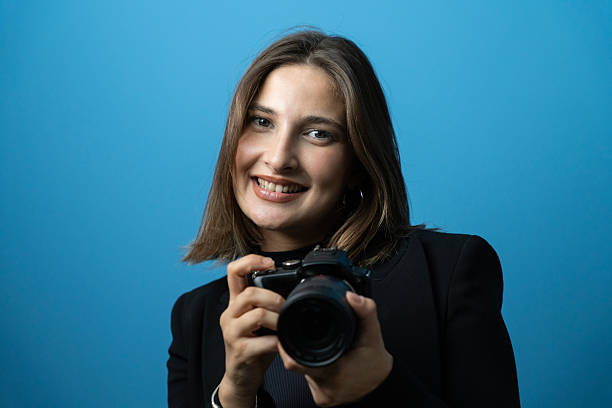 istock Smiling Young Woman Holding Professional Camera Against Blue Background 2234918372