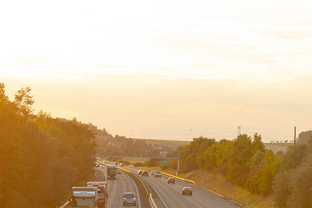 A scenic highway with multiple cars driving down it during a beautiful sunset, showcasing the vibrant colors of the evening sky