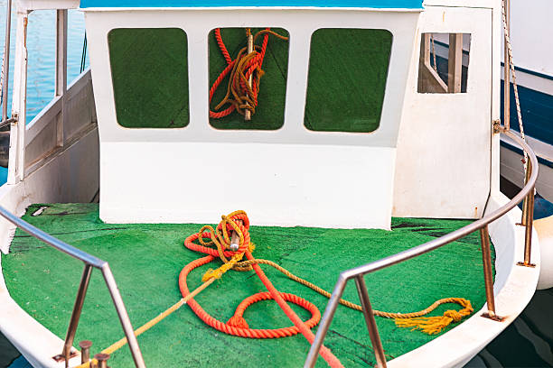 Small boat deck with green flooring, colorful ropes neatly arranged, and a simple cabin structure. Nautical details highlight maritime life, boating equipment, and seaside charm