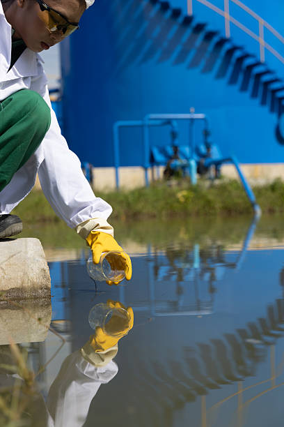 istock Young science Biologist or environmental quality inspector wearing protective gear and white lab coat collecting water sample from Sedimentation pond , water treatment facilities 2234943961