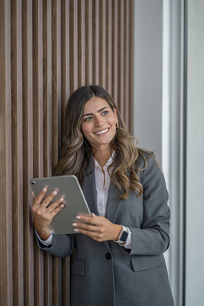 istock Smiling businesswoman using digital tablet leaning against wall in modern office 2234948778