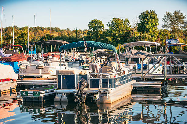 The Poonton boat was taken on the Milles-ïles river in Laval, Québec Canada.  The season is summer, the trees are green.  The pootoon boat is mooring at the cedar floating dock, in front of the dock there is a small island.  The boat is having a Bimini top.