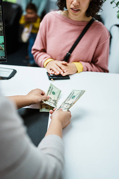Cropped view with selective focus on the hands of an unrecognizable female bank teller as she counts US currency for an Eurasian female customer.