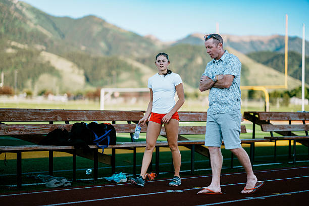 A coach provides guidance and feedback to a female collegiate track and field athlete during a summer training session at the rural school stadium.