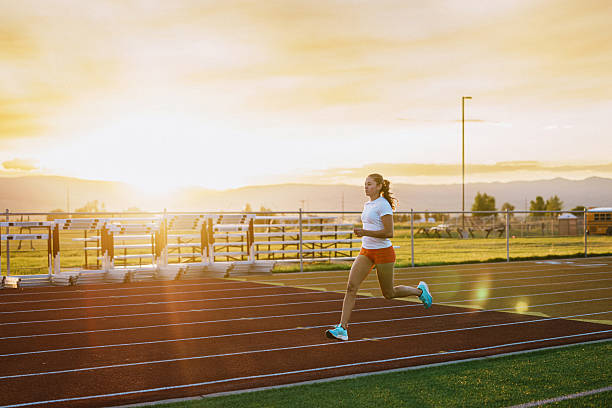 A female collegiate track and field athlete runs at speed along the school stadium track during a sunset training session.