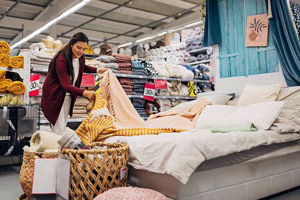 istock Asian woman browsing through discounted home textile items such as bedspreads, blankets, and cushions in a modern furniture store 2234954900
