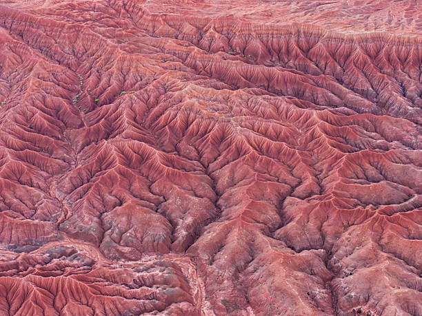 An aerial view of the Painted Desert in Arizona, where vivid red earth is carved into intricate ridges and gullies, creating a striking natural pattern shaped by erosion.