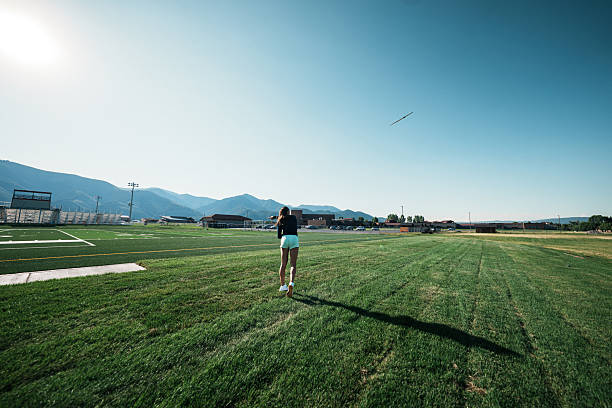A female collegiate heptathlete watches her javelin soar across the field after a powerful throw during training.