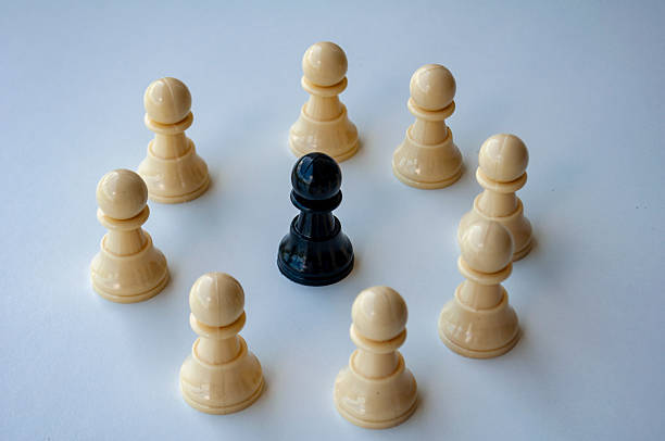 Multiple beige pawns surrounding a black king chess piece on a clean surface conveying themes of protection, power, or opposition.