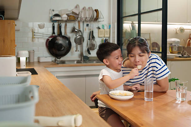 istock A young Asian boy lovingly feeds his mother during breakfast, showing affection as they enjoy their morning meal together in the kitchen. 2234962242