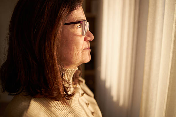 istock Senior woman looking through the window 2234962591
