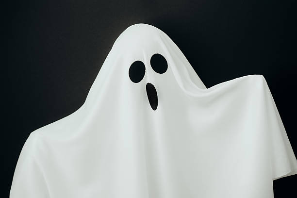 Surprised white ghost costume with dark holes for eyes on black background