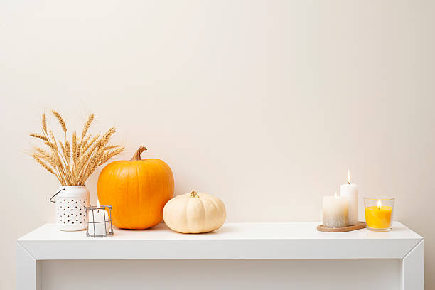 istock Pumpkins and burning candles on white pedestal surface in light room interior background 2234968605