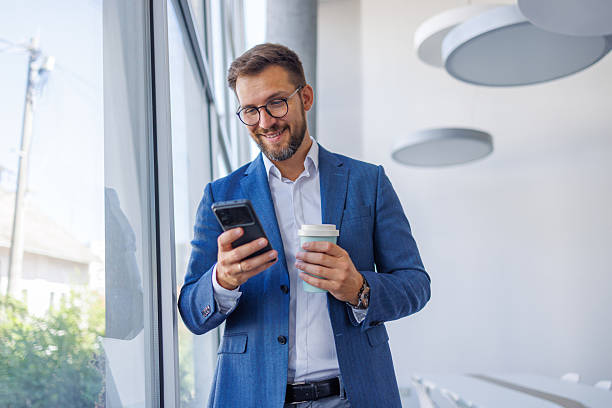 istock Smiling businessman using smartphone and drinking coffee in office 2234968668