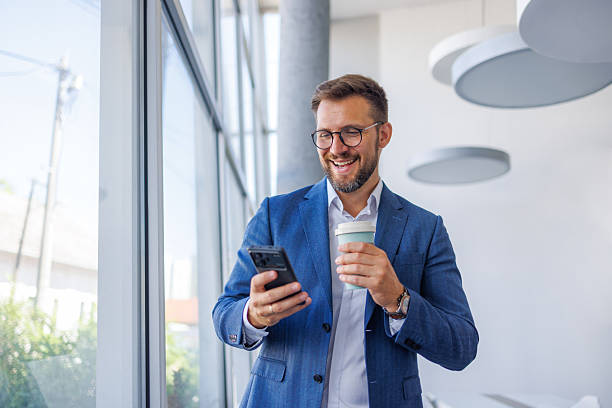 istock Smiling businessman using smartphone and drinking coffee in office 2234968742