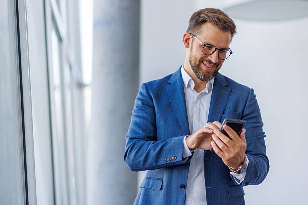 istock Smiling businessman using smartphone in office corridor 2234968780