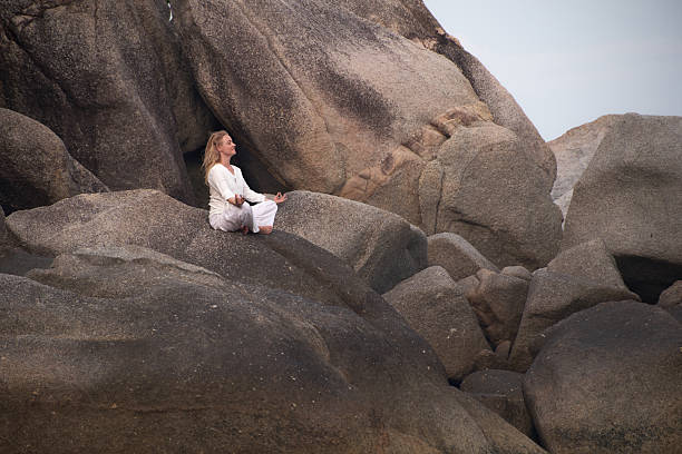 Carefree woman exercising Yoga in Lotus position during summer day on a rock. Photographed in medium format.
