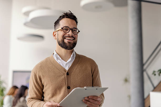 istock Smiling Businessman in Brown Sweater Holding Clipboard in Bright Modern Office Setting 2234989750