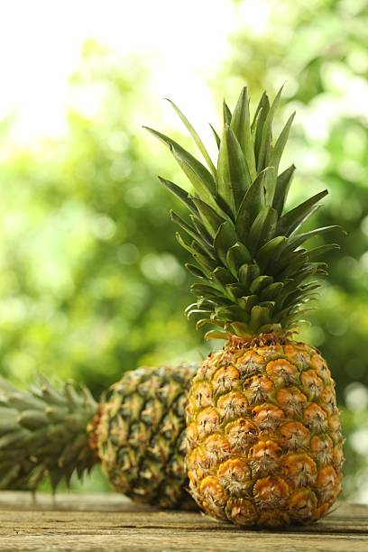 istock Fresh ripe pineapples on wooden table against blurred background 2234994344