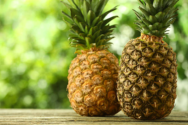 istock Fresh ripe pineapples on wooden table against blurred background, space for text 2234994448