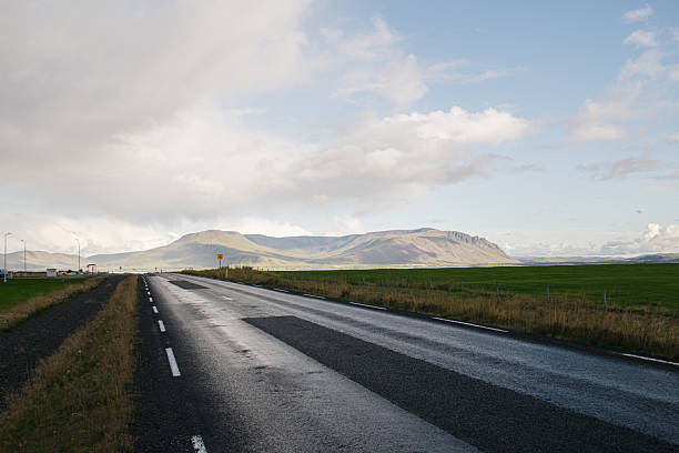 A serene road through Akranes countryside and scenic mountains under a partly cloudy sky.