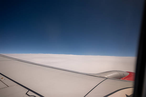 Airplane wing soaring above a blanket of clouds, with a clear blue sky