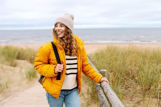 istock A happy woman in a bright yellow jacket stands on a sandy beach. 2234999639