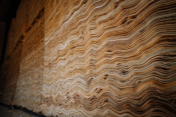Close-up view of stacked wavy veneer wood sheets with natural textures and patterns inside a woodworking or plywood production facility.
