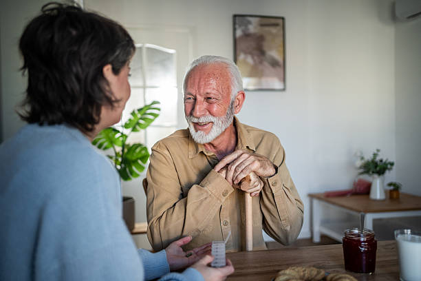 istock Senior man smiling while talking with nurse holding pills at home 2235000494