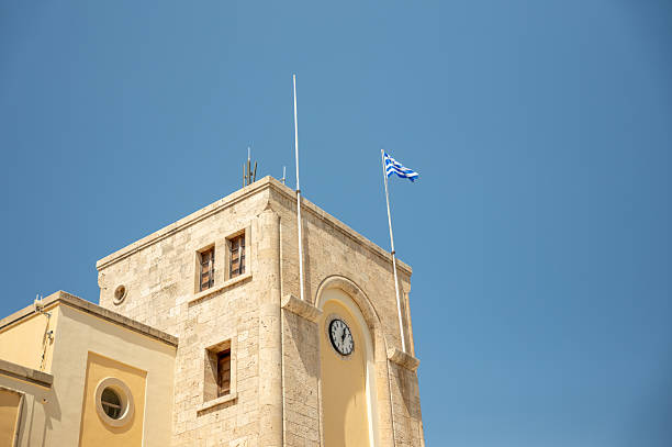 Greek flag waving on a clock tower under blue sky