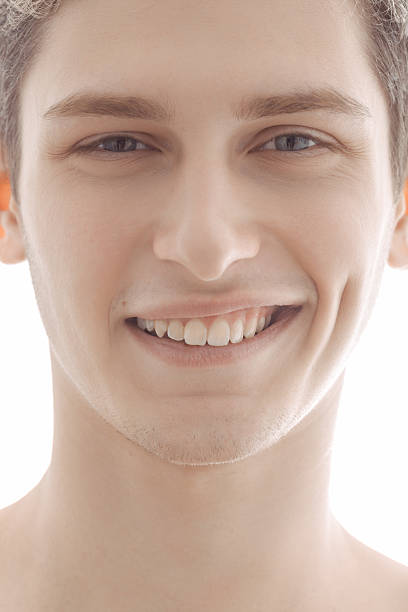 A close-up portrait of a young man smiling warmly, showcasing natural charm and confidence, illuminated by soft, bright light against a white background. Ideal for lifestyle or beauty themes.
