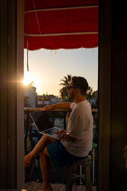 istock Young man working on laptop at sunset on balcony 2235003780