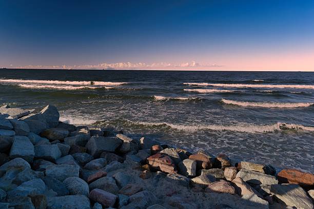istock Waves crash on rocky shore during twilight near coastal landscape 2235003960