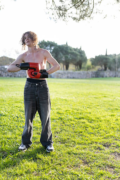 Top view of a sportsman in red sneakers, gray sports shorts and black t-shirt doing warm up exercises with resistance band. Athletic man exercising outdoor with fitness band. Sport and people concept