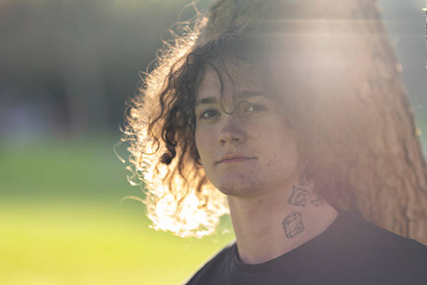 istock Young man with curly hair and tattoos posing outdoors in sunlight 2235006940