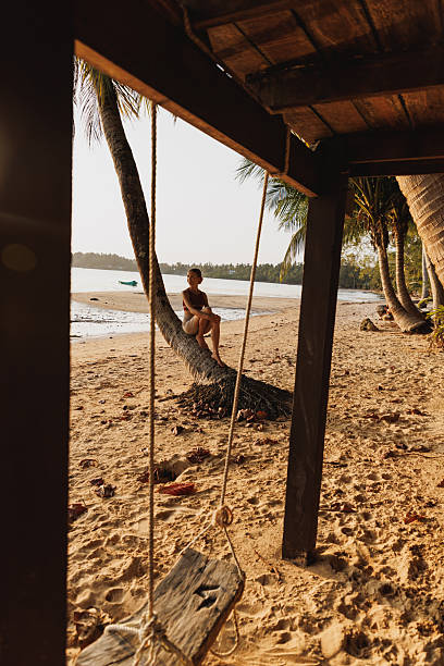 Person relaxing on a palm tree by a tropical beach under a warm sunset