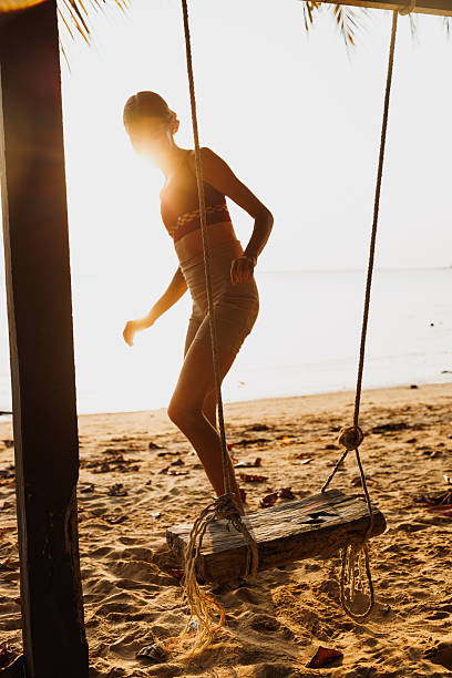 istock Woman enjoying a sunset on a beach swing under a tropical palm tree 2235009483