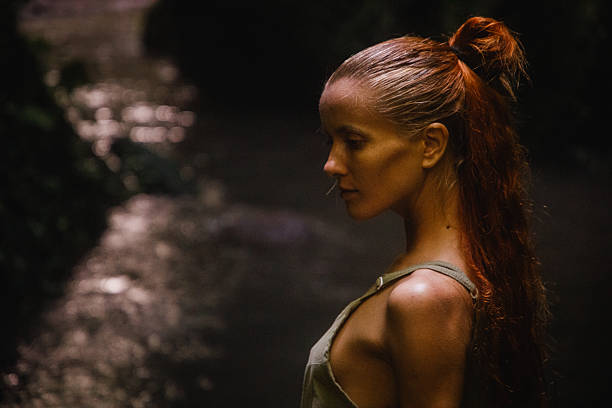 istock Woman with red hair posing by a tranquil water setting at night 2235012006