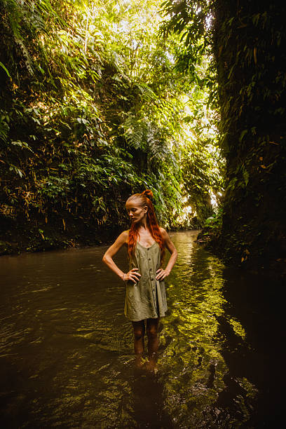 istock Woman standing confidently in a serene jungle stream surrounded by lush flora 2235012015