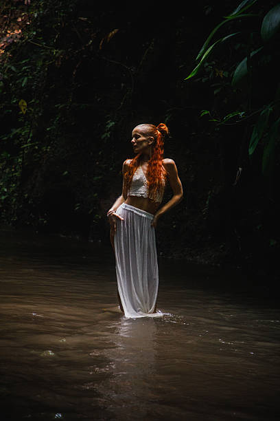 A young teenage girl in a white dress stands in a lake against a background of green foliage. day Ivan bathed.