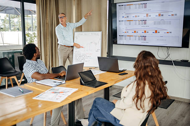 istock Small group of people having a business meeting using laptops while one businessman is presenting actions they need to take using white board 2235012585