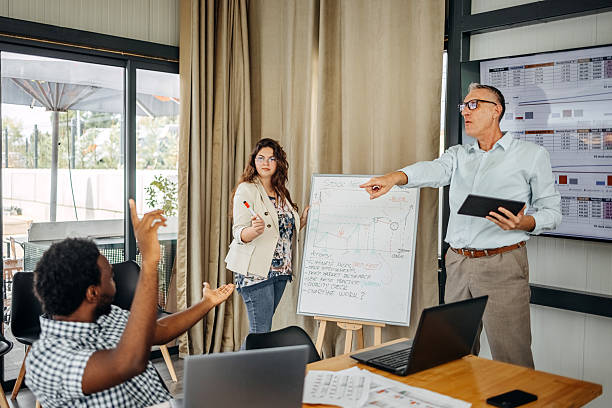istock Small group of people having a business meeting using laptops and brainstorming in front of white board 2235012653