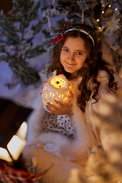 girl in a white fur cape sits in a winter studio, holding a glowing lantern. The magical scene with twinkling lights, toy polar bear, snowy trees. Holiday themed projects, cards, and festive decor