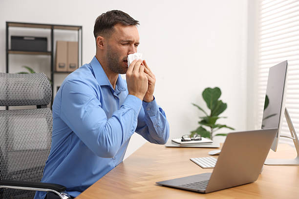 istock Sick man with runny nose at table in office 2235013381