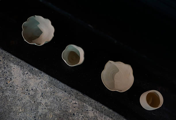Four handmade ceramic cups and bowls placed on a dark, glossy countertop.