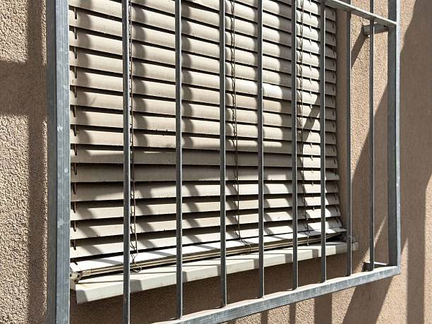 istock Sunlit exterior window with metal bars and closed blinds 2235017380