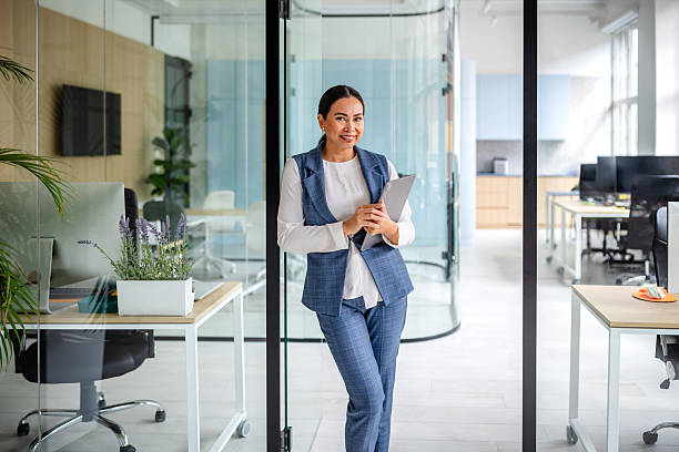 istock Confident businesswoman standing in a modern office space while holding a tablet and smiling 2235027336